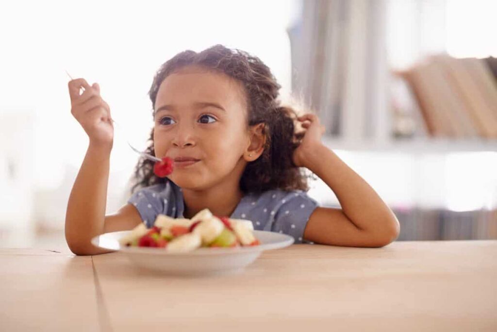 Young girl sitting at table eating fruit