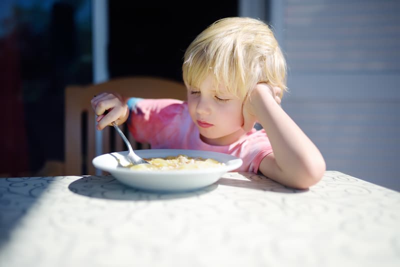 Image of a young toddler looking disappointed as they hold a spoon in their bowl of cereal