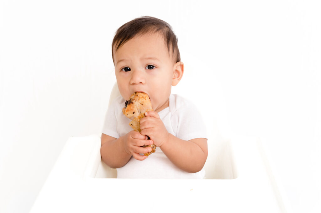 Baby in high chair eating chicken drumstick