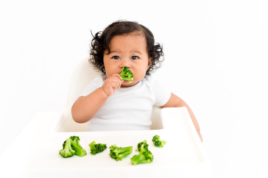 Baby in high chair with broccoli