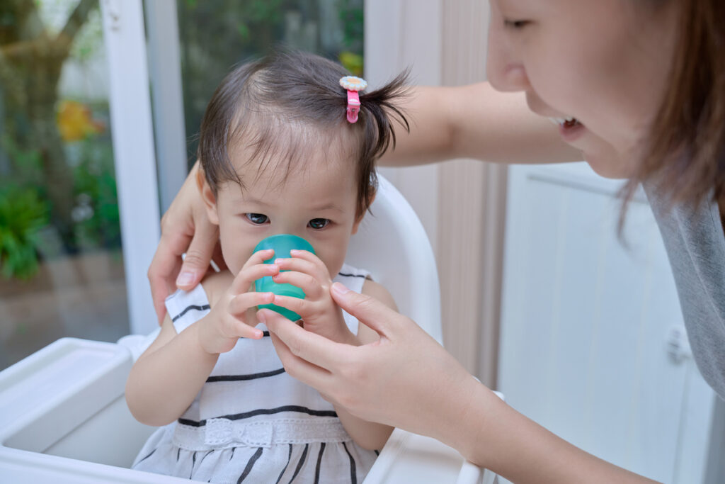 Parent helping baby drink from cup