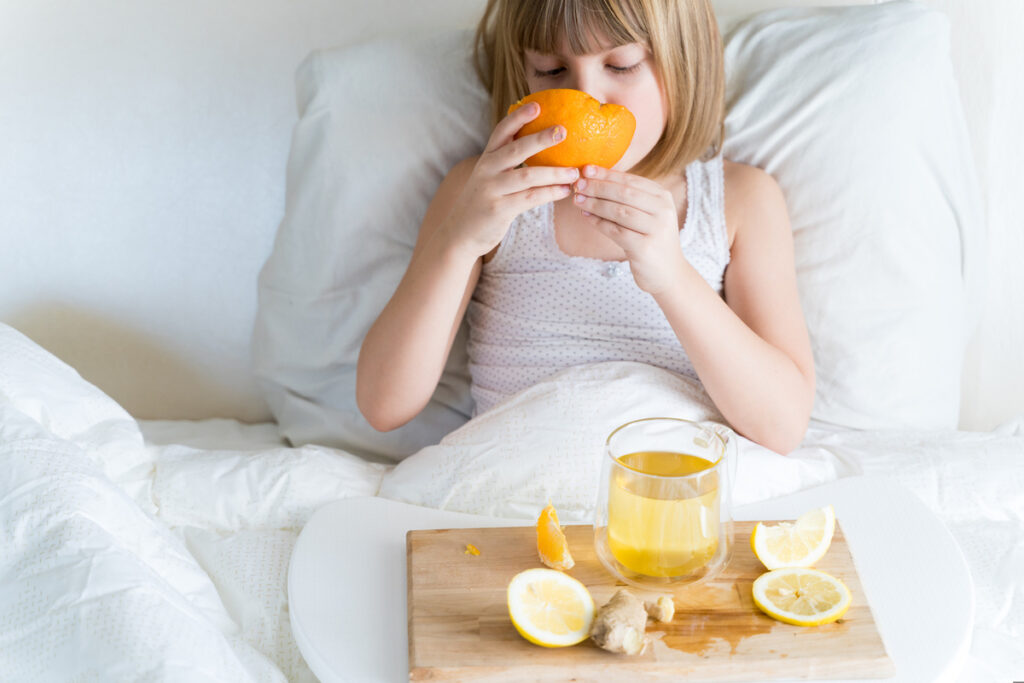 Sick child in bed with tray of vitamin C foods and cold remedies