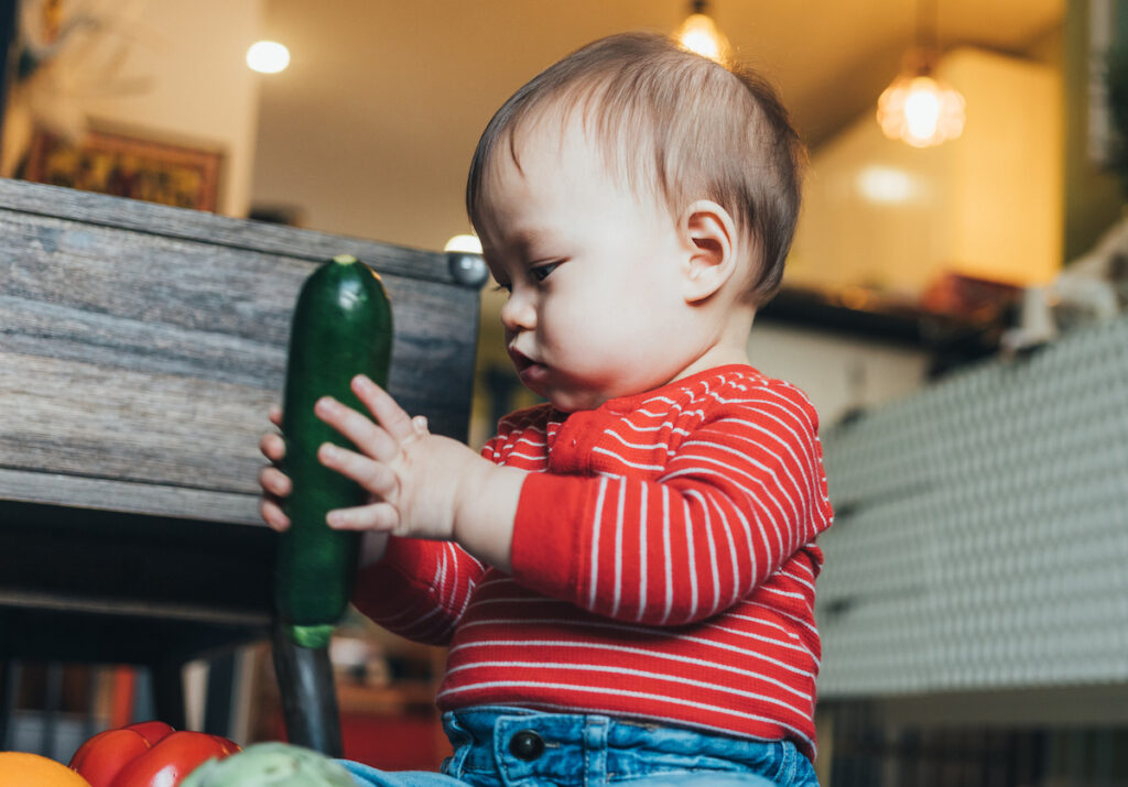 Baby holding a zucchini toy