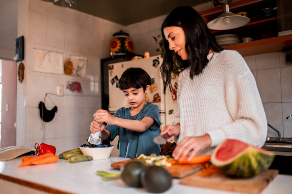 Child seasoning food with salt while cooking with mom