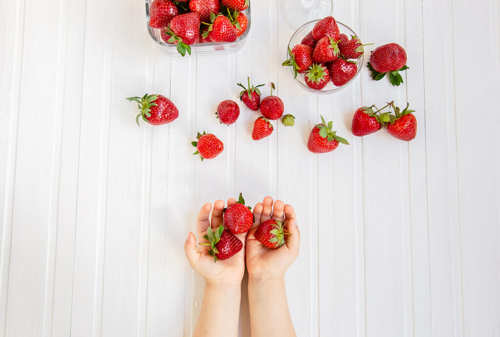 A child's hands holding strawberries with more scattered around