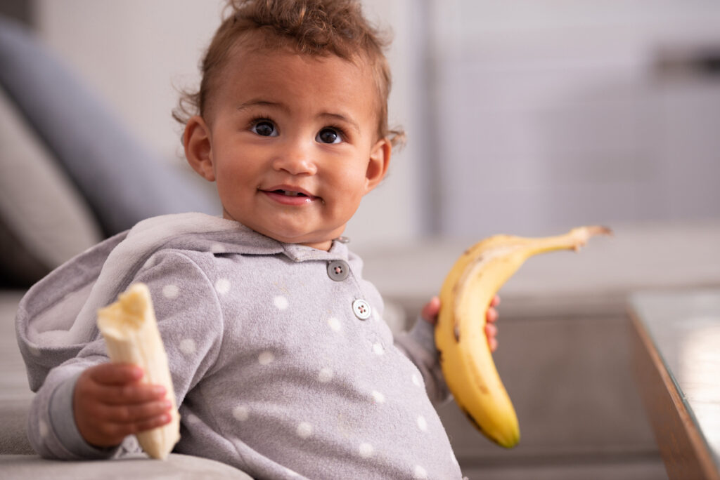 Baby holding two bananas in their hands