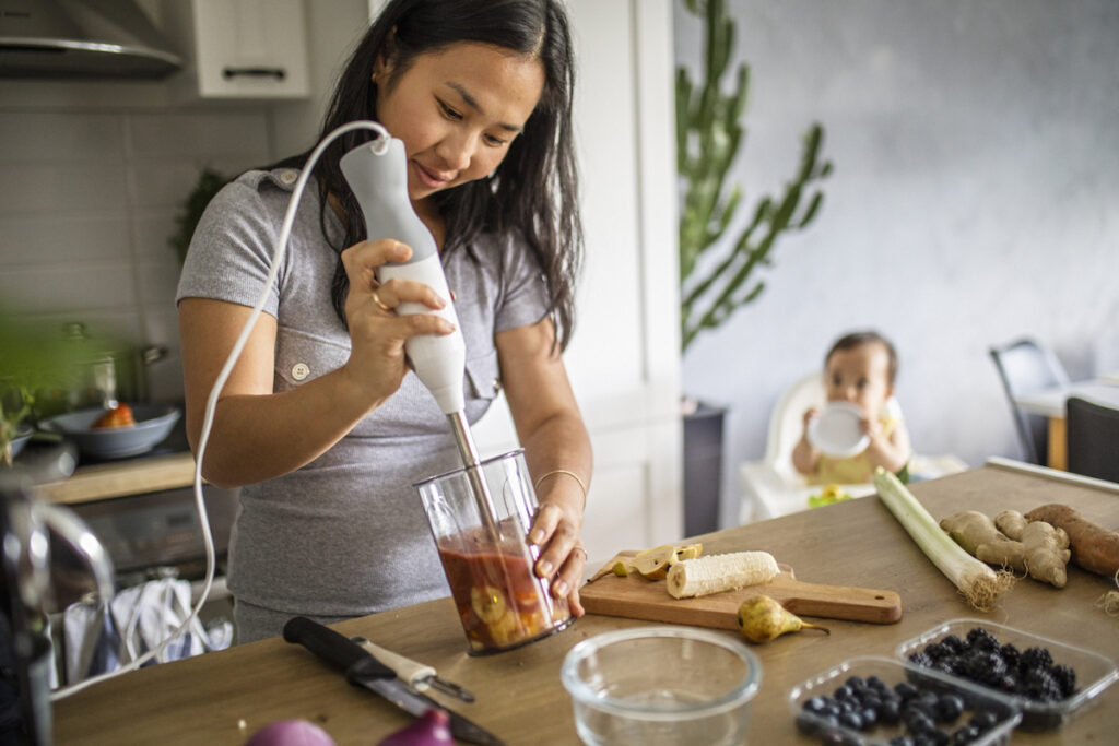 Mother using handheld blender to puree food for baby