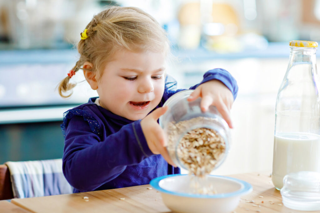 Toddler is pouring oats into a bowl preparing a fiber-rich meal