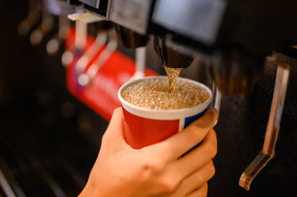 A soda machine pours a soft drink into a cup being held by a child