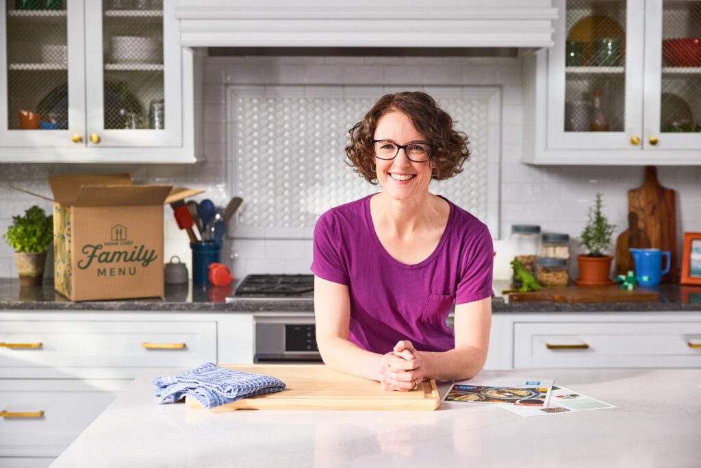 Jennifer leaning on the kitchen counter with a Home Chef box in the background. 